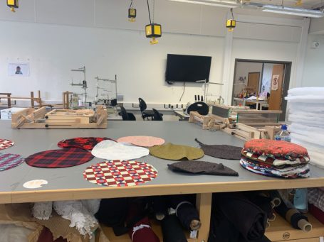 A workspace with various fabric circles and sewing equipment scattered on a table.