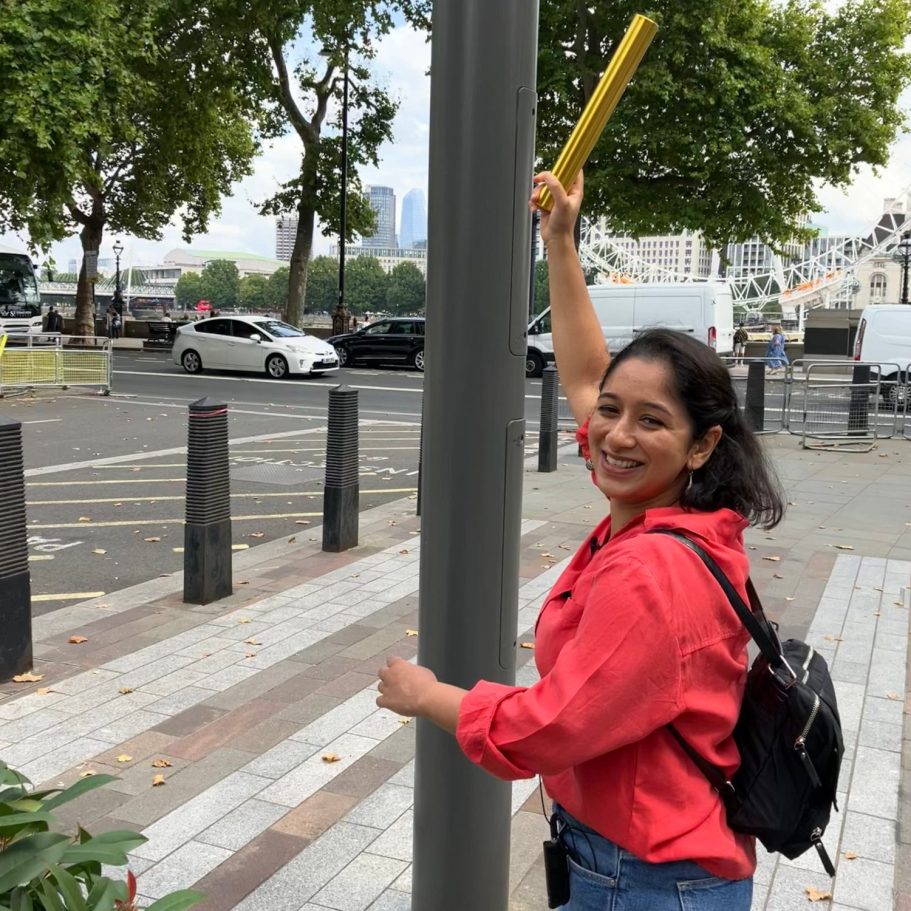 A woman in a red shirt, blue jeans and black backpack leading a guided tour on the streets of London